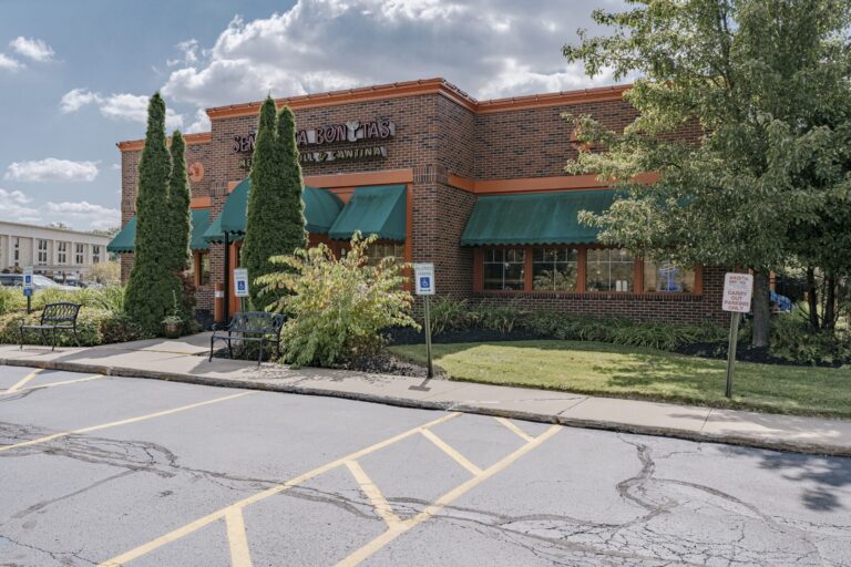 Exterior of a brick Mexican restaurant with green awnings on a sunny day, surrounded by greenery and a parking lot with handicapped signs.